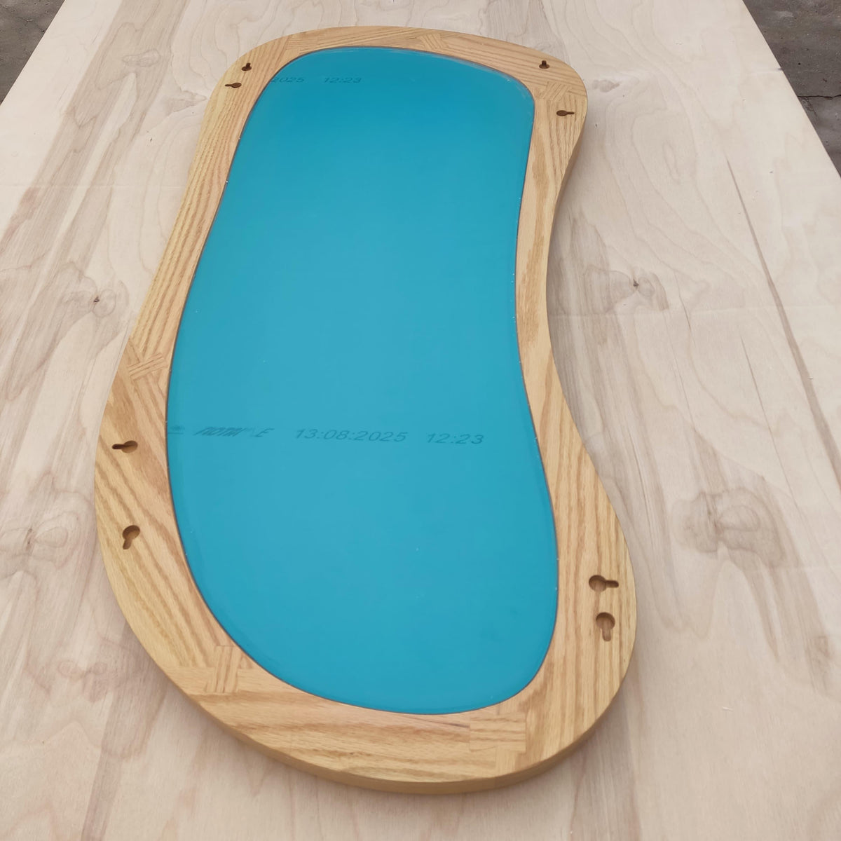 May include: A uniquely shaped mirror with a light blue surface, framed by a light-colored wooden border. The frame has a natural wood grain and includes mounting hardware. The mirror's shape is irregular, with rounded edges. The text "13.08.2025 12:23" is visible on the surface.