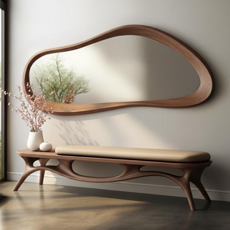 May include: A modern, organic-shaped wooden mirror with a matching bench. The mirror has a unique, flowing frame and is mounted above the bench. The bench features a cushioned seat and a sculptural wooden base. A vase of flowers sits on the bench.