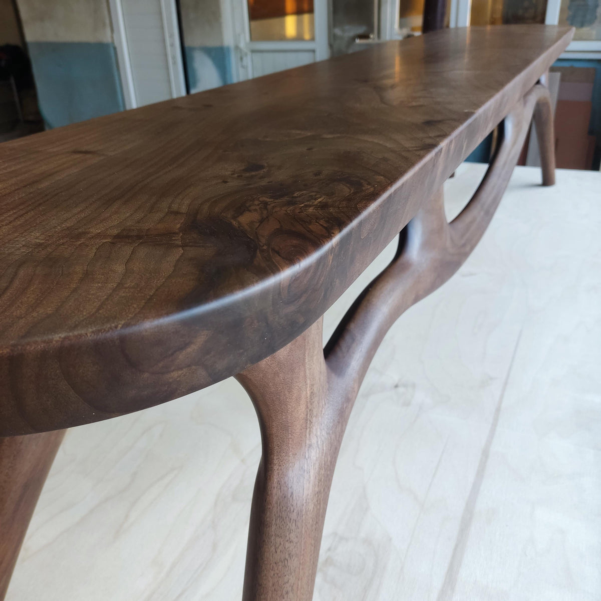 May include: A long, dark brown wooden bench with a smooth, polished surface. The bench has a unique design with curved legs and a natural wood grain pattern. The bench is approximately 72 inches long.
