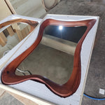 May include: A wooden framed mirror with a unique, wavy design. The frame is a rich, dark brown color, and the mirror is rectangular with curved edges. The mirror is packaged in a white foam-lined box, suggesting it is new and ready for use.
