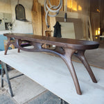 May include: A handcrafted, dark brown wooden bench with a unique, organic design. The bench features a long, curved seat supported by intricately carved legs. The bench is approximately 72 inches long.