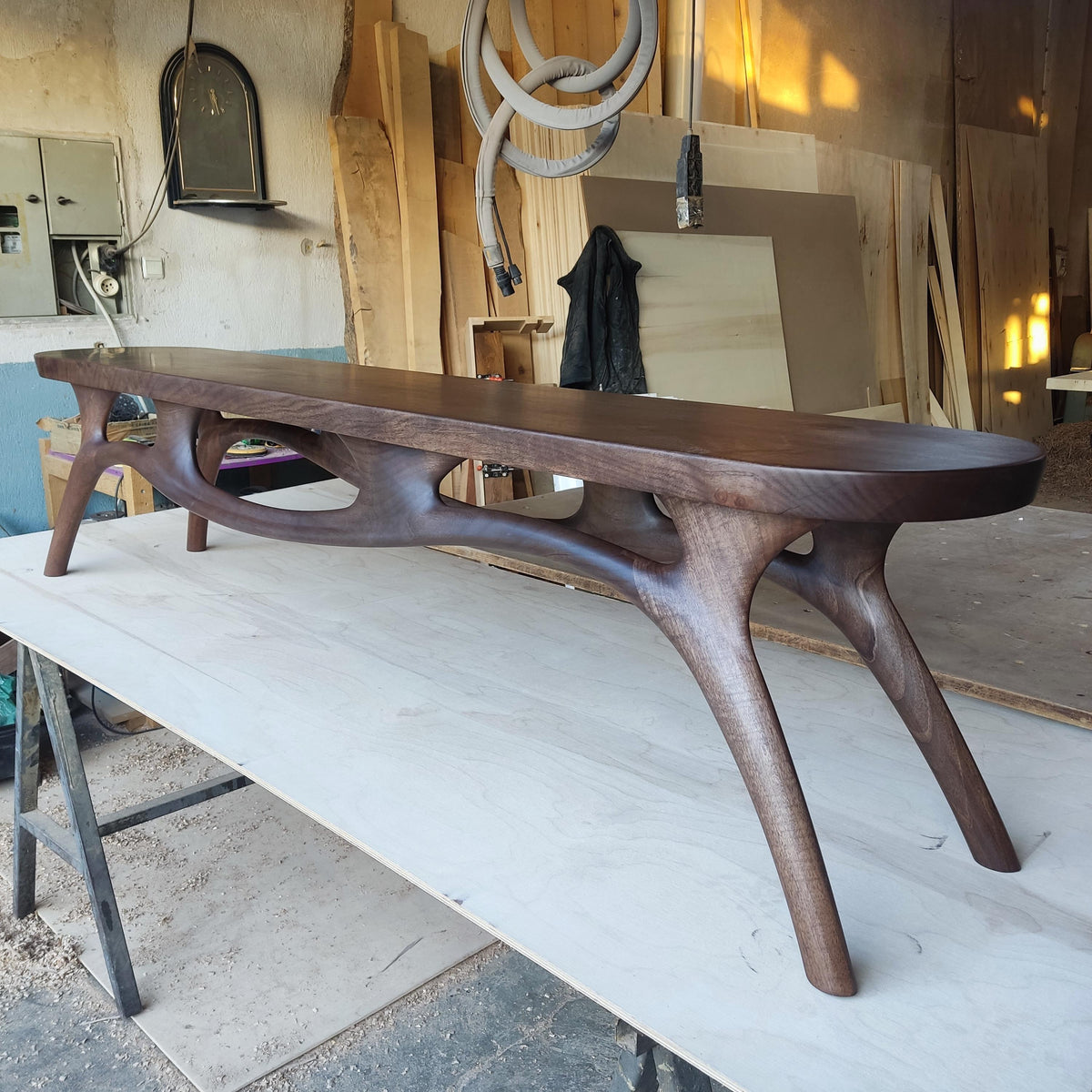 May include: A handcrafted, dark brown wooden bench with a unique, organic design. The bench features a long, curved seat supported by intricately carved legs. The bench is approximately 72 inches long.