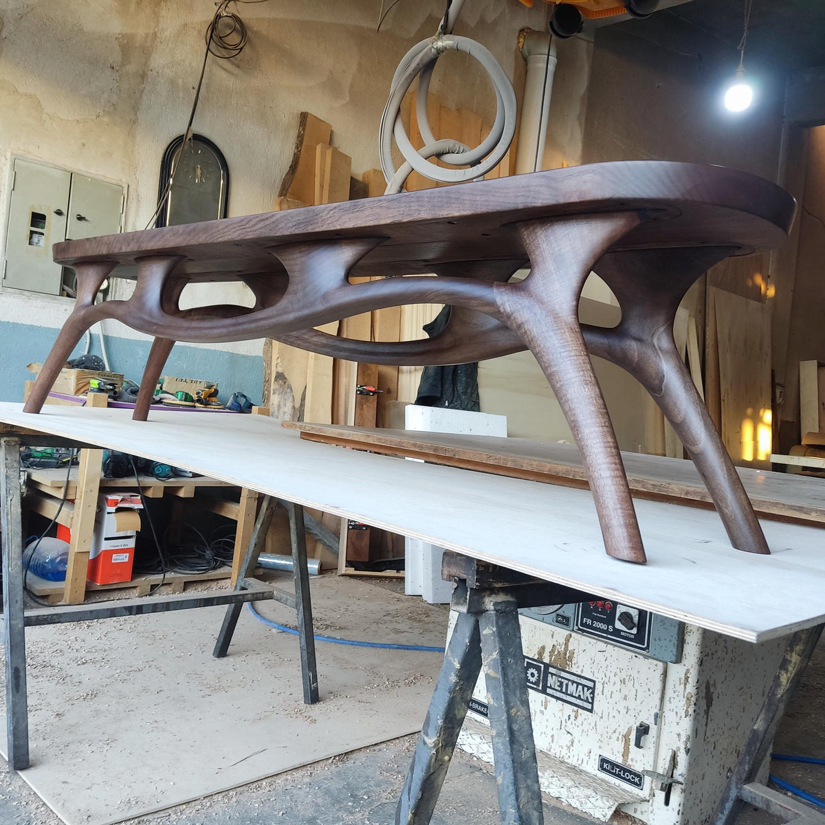 May include: A dark brown, handcrafted wooden table with a unique, organic design. The table features a smooth, oval-shaped top and intricately carved legs, showcasing a modern aesthetic. The table's dimensions are approximately 72 inches long, 30 inches wide, and 18 inches high.