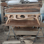 May include: A light-colored wooden bench with a curved design and a gray cushion. The bench has four legs and a unique, openwork design in the center. The bench is approximately 60 inches long.