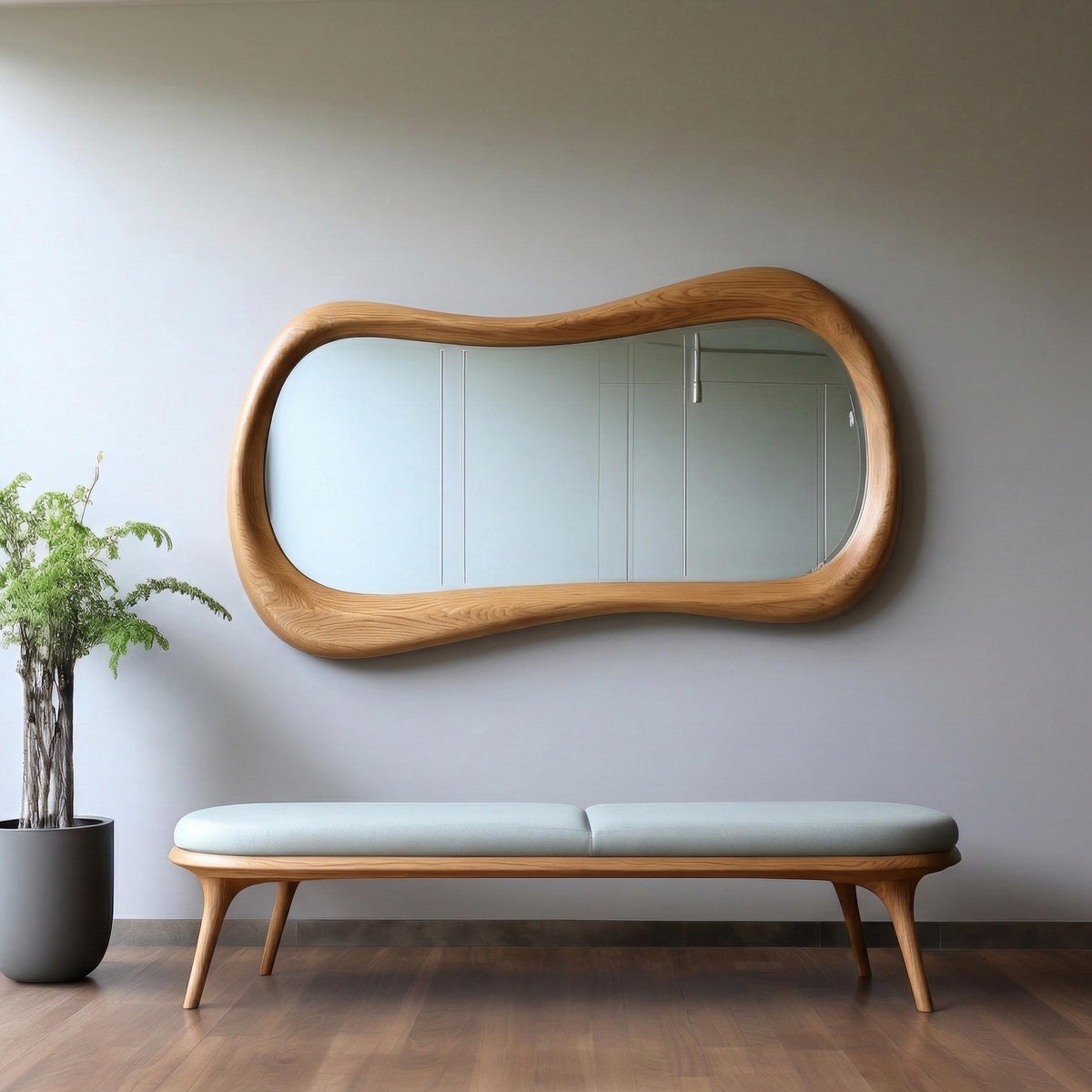 May include: A wall-mounted mirror with a thick, light-toned wooden frame featuring an irregular, organic, wavy shape. Below the mirror sits a long, rectangular bench with a light gray upholstered seat and a light-toned wooden base.