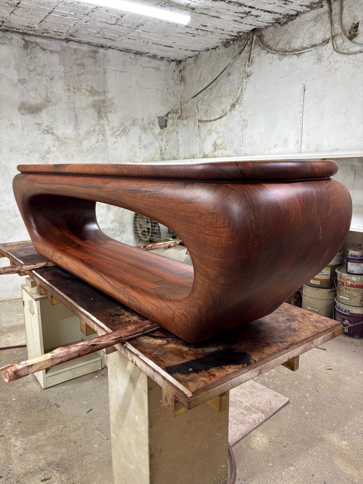 May include: A handcrafted, solid wood coffee table with a rich, reddish-brown finish. The table features a unique, organic design with a curved, flowing form and an open center. The table is approximately 60 inches long.