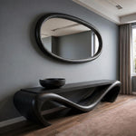 May include: A dark wood console table with a wavy design and a matching oval mirror. A black bowl sits on the table. The furniture is set against a gray wall and hardwood floor.
