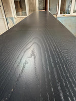 May include: A close-up view of a long, rectangular, black wooden surface with a visible wood grain pattern. The surface appears to be smooth and polished, with a slight sheen. The wood grain has a natural, organic appearance.