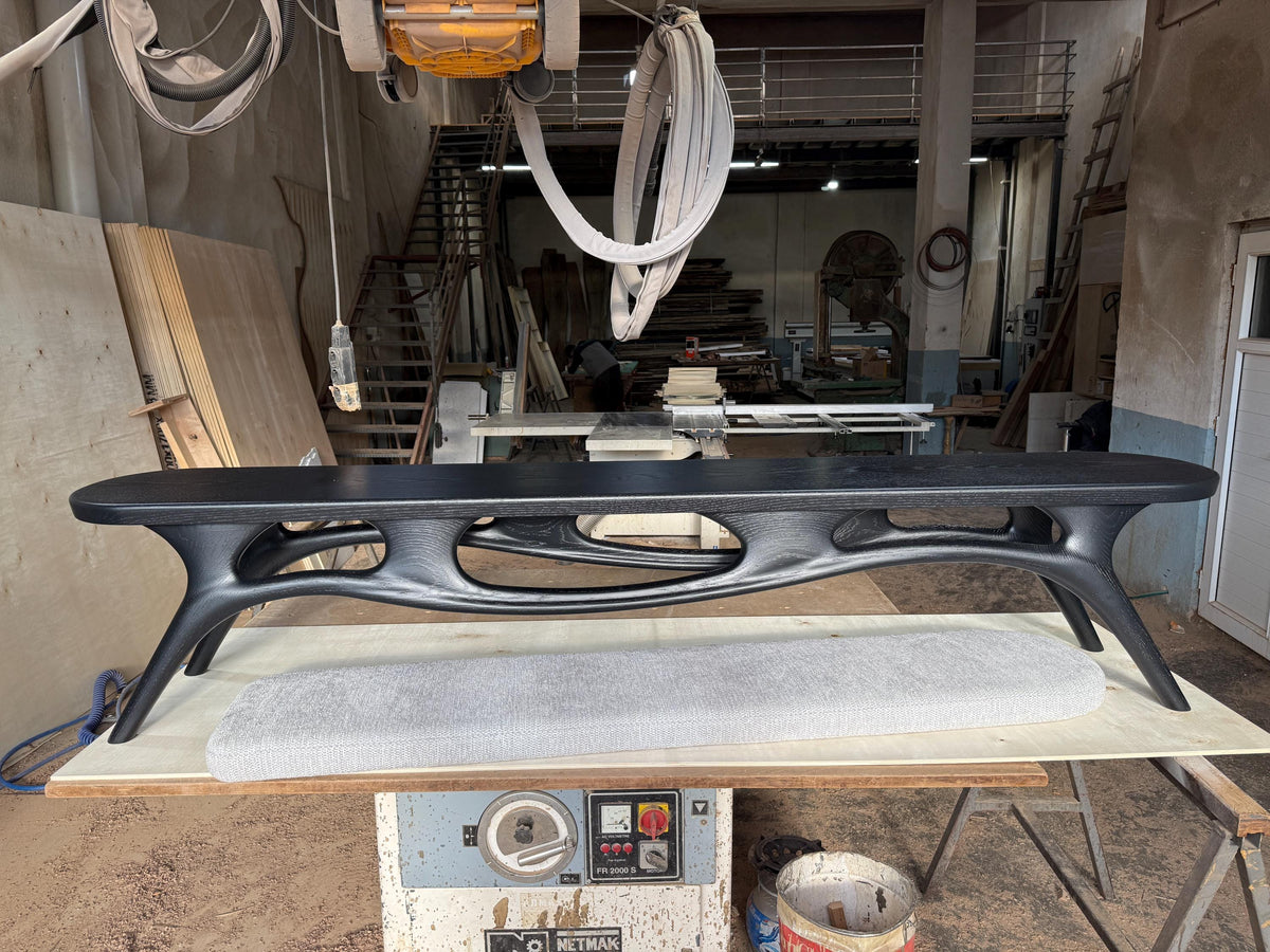 May include: A black, modern-style coffee table with an oval top and unique, open-work legs. The table is approximately 72 inches long and sits on a light-colored surface. The design features a blend of curves and angles.