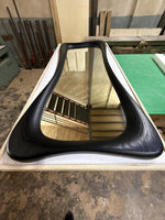 May include: A black, organically shaped mirror with a wooden frame. The mirror is set in a wooden box with white padding. The reflection shows a staircase. The frame has a smooth, curved design.