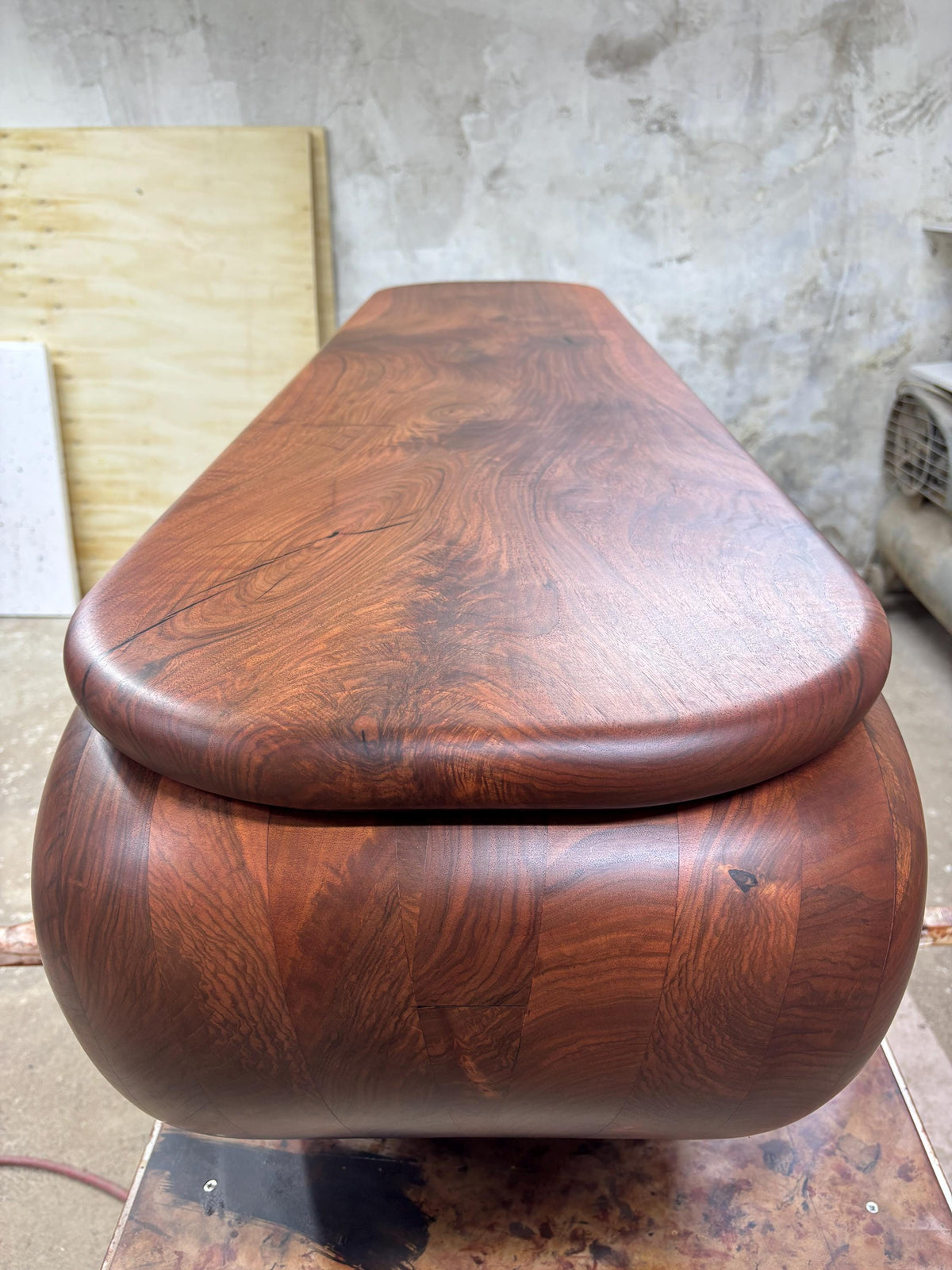 May include: A handcrafted wooden box with a rounded, oval shape and a matching lid. The box is made of dark brown wood with a visible grain pattern. The lid sits flush on top of the box.