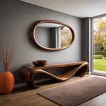 May include: A modern, wooden console table with a unique, flowing design. Above it hangs an oval-shaped mirror with a wooden frame. A wooden bowl sits on the table. An orange vase with branches and a brown rug complete the room's decor.