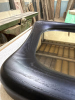 May include: Close-up of a black, curved wooden frame with a rectangular opening. The wood grain is visible, and the frame has a smooth, polished finish. The frame appears to be part of a larger piece, possibly a mirror or a window.