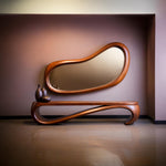 May include: A modern, wooden console table with a matching, organically shaped mirror. The mirror and table are made of a warm-toned wood. Two dark brown decorative vases sit on the table.