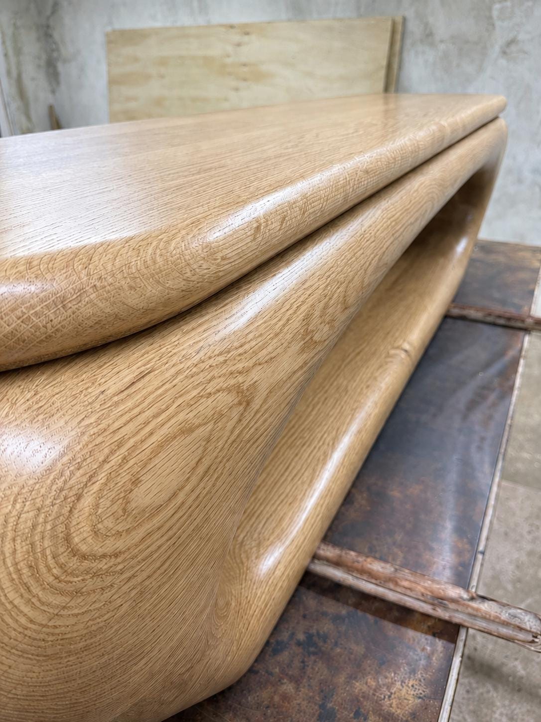 May include: A light-colored wooden table with a curved, flowing design. The table has a smooth, glossy finish and visible wood grain. The design features a unique, open space in the center, adding a modern touch to the furniture.