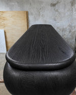 May include: A dark charcoal-colored wooden decorative urn with a rounded base and a conical lid. The wood grain is visible, adding texture to the piece. The urn has a smooth, polished finish, suggesting it is a handcrafted item.