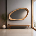 May include: A wall-mounted mirror with an asymmetrical, organic wooden frame featuring a light natural finish. Below the mirror sits a long, low bench with a light-colored upholstered seat, a wooden frame, and four tapered wooden legs.