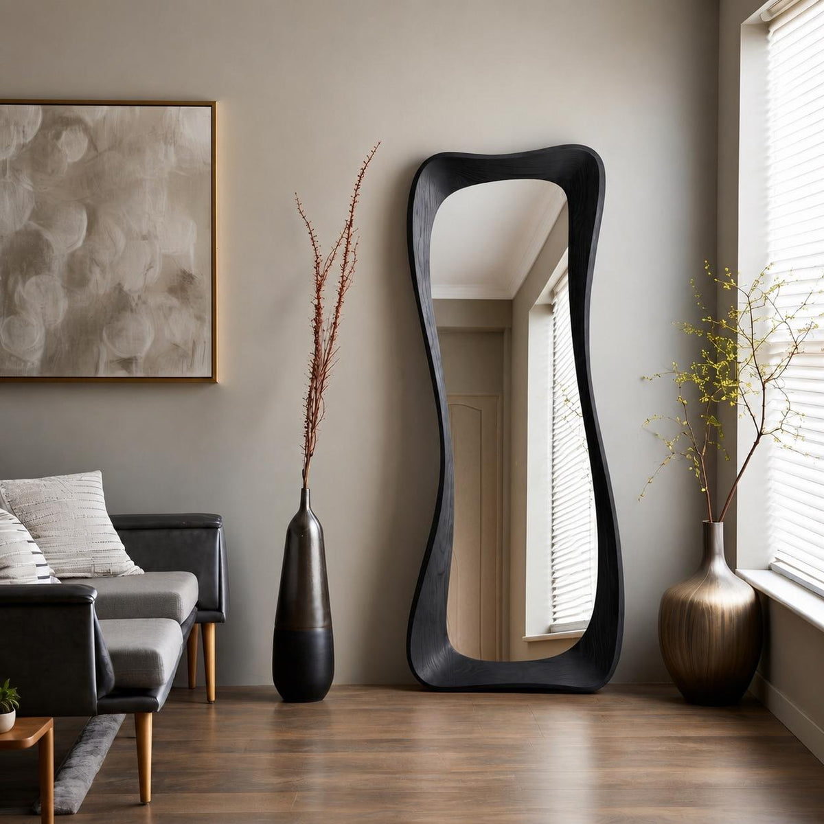 May include: A tall, floor-standing mirror with a dark, irregular, organic-shaped wooden frame. The mirror is positioned between two decorative vases, one tall and slender with dried branches and one rounded with green foliage, near a sofa.