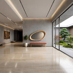 May include: A large, irregularly shaped wooden-framed mirror mounted on a gray wall above a long, low bench with a red cushion. The space features polished light-colored stone flooring, recessed ceiling lighting, and a view of a garden.
