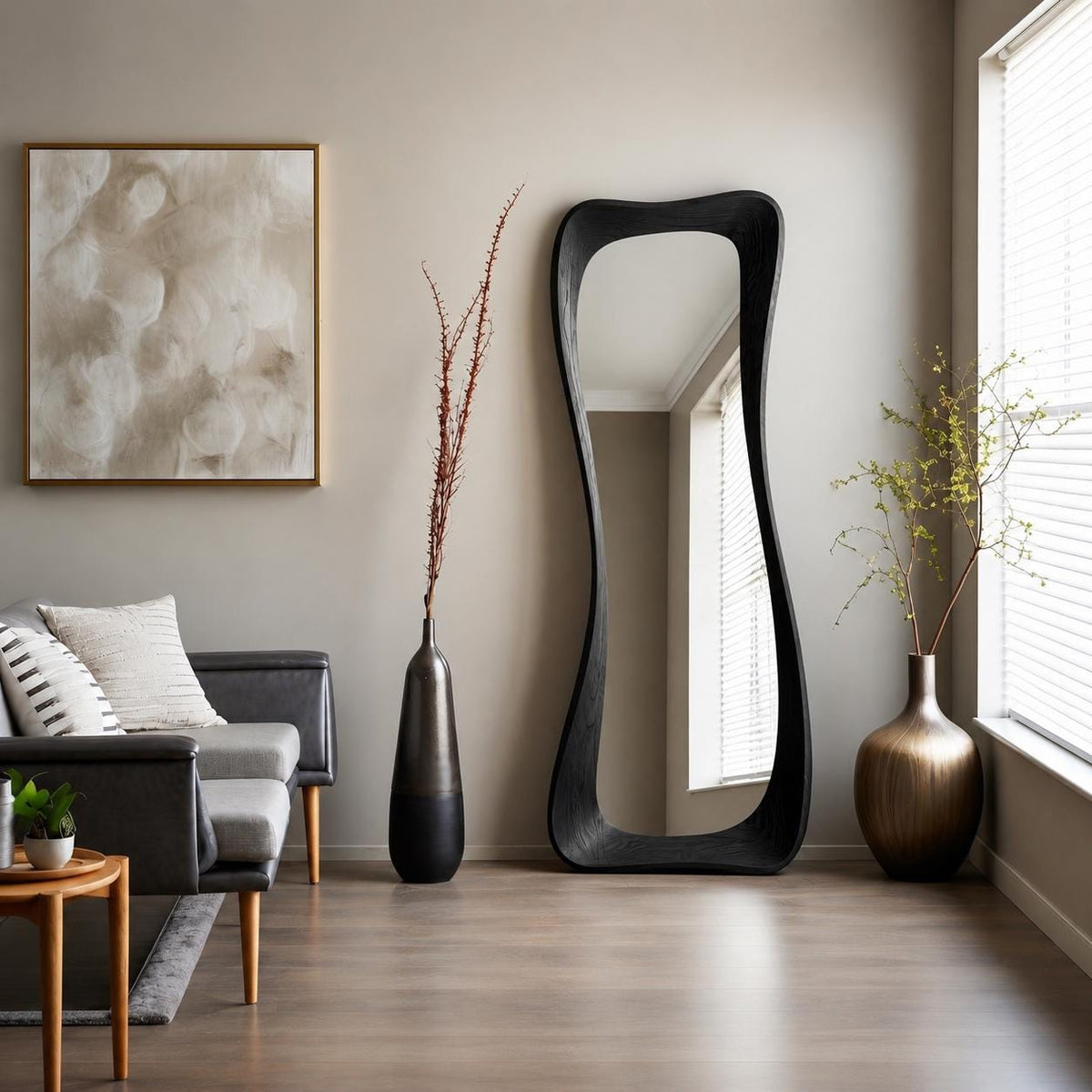 May include: A tall, floor-standing mirror with a thick, black, wavy, organic-shaped frame. The mirror is positioned upright against a neutral-colored wall, reflecting the interior space, including a window with white blinds and light-colored walls.