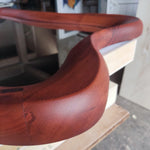 May include: A curved, reddish-brown wooden frame with a smooth, rounded surface and visible wood grain. The structure features a continuous, flowing shape with distinct joints where segments of the wood meet, showcasing a polished finish.