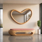 May include: A wall-mounted mirror with a thick, light-toned wooden frame in an irregular, organic bean shape. Below it sits a matching wooden bench with a smooth, rounded base and a long, rectangular cushion in a soft, muted pink color.